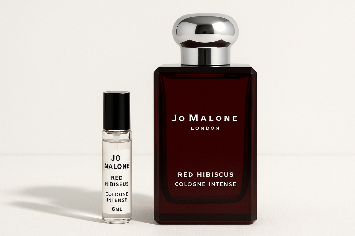 Mostră de 6 ml Jo Malone Red Hibiscus Cologne Intense, așezată lângă sticla de parfum de 100 ml Jo Malone Red Hibiscus Cologne Intense, care are scris alb pe sticla roșu închis.